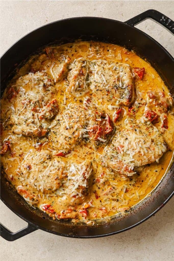 Creamy sun dried tomato chicken thighs in a cast-iron skillet atop a marble countertop.