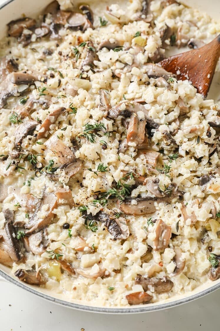 Cauliflower Risotto With Mushrooms with a wooden spoon on a pan atop a marble countertop.
