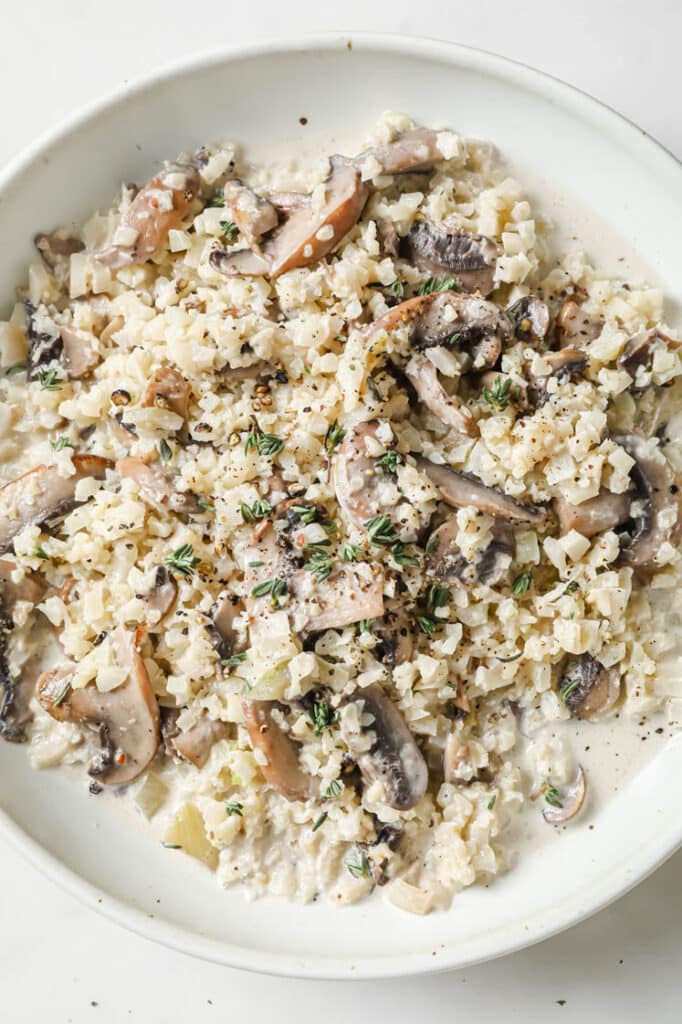 Cauliflower Risotto With Mushrooms on a shallow bowl atop a marble countertop.