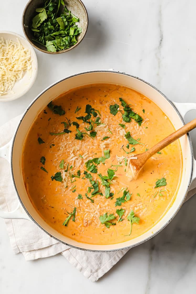 Garnished creamy Italian sausage soup in pot with a wooden spatula and garnishes on the side.