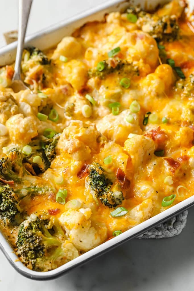 Cheesy broccoli cauliflower casserole with a spoon in it on a hot pad.