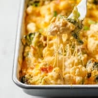 Loaded Broccoli Cauliflower Casserole on a baking dish with a portion on a fork atop a marble countertop.