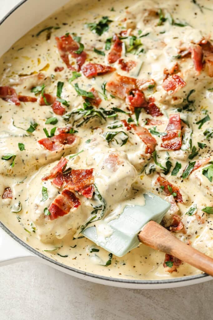 Garnished creamy dijon chicken in a white pan with a spatula scooping out a portion.