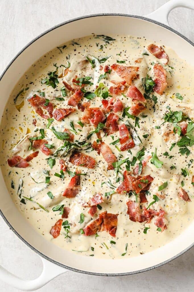 Garnished creamy dijon chicken on a white pan atop a marble countertop.