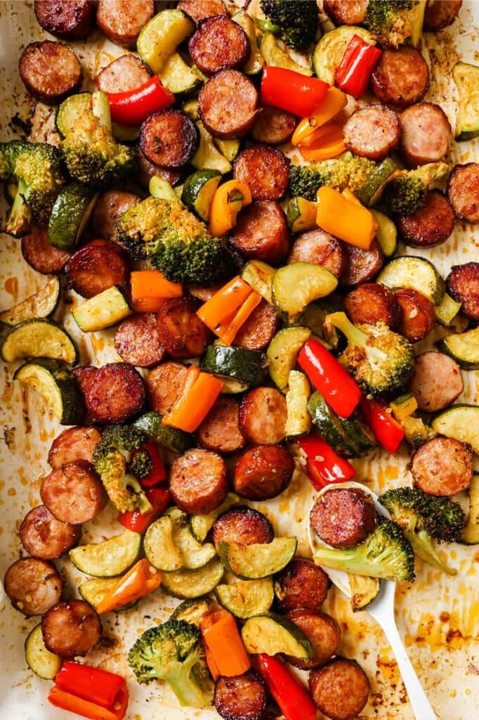 Sausage and veggies sheet pan dinner with a spoon.