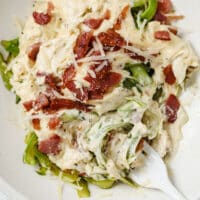 A plate of asparagus noodles with alfredo sauce and bacon with a fork.