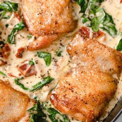 Close-up of creamy Tuscan chicken in an iron skillet.