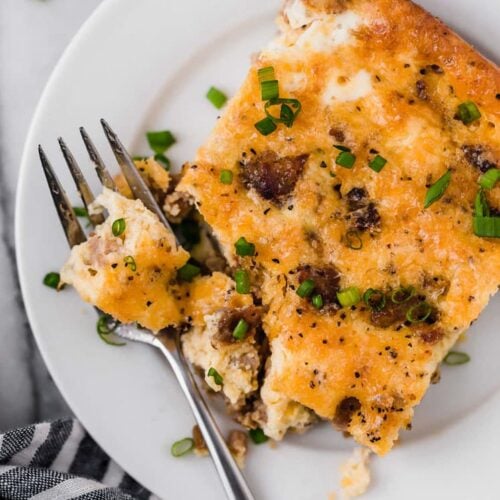 A slice of sausage breakfast casserole on a plate with a fork.