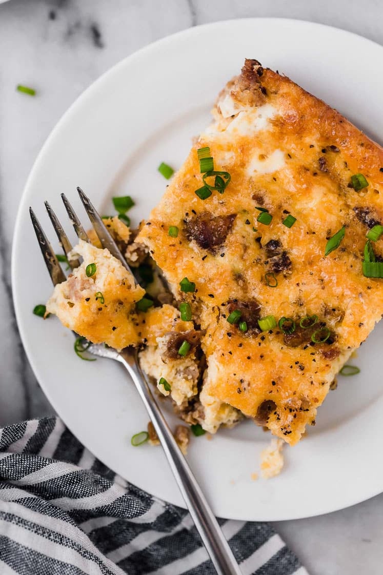 A slice of sausage breakfast casserole on a plate with a fork.