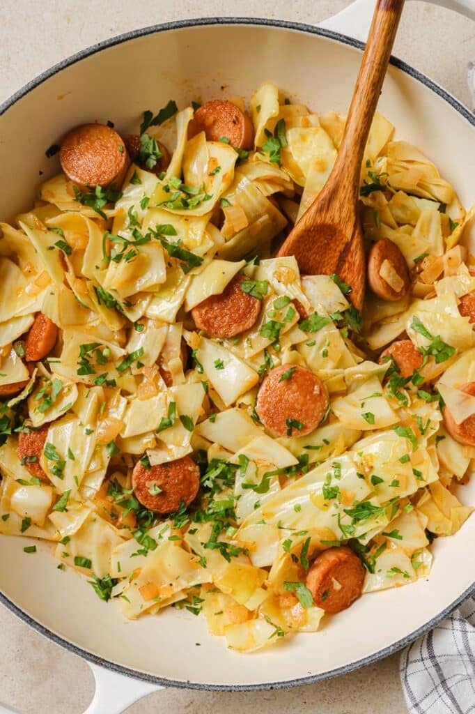 Cabbage and sausage on a pan with a wooden spoon.