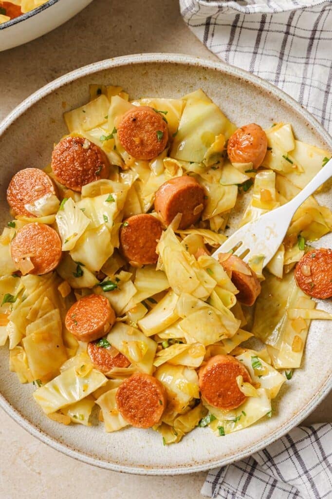 A serving of cabbage and sausage on a plate with a fork.