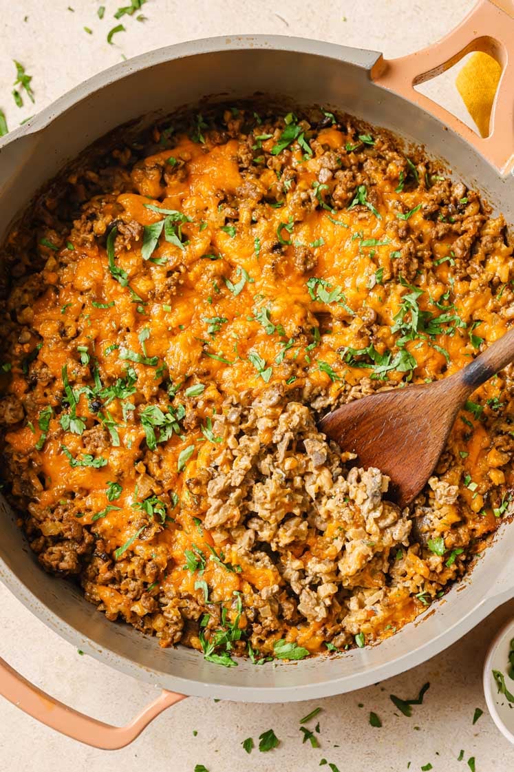 Creamy ground beef skillet with cauliflower rice on a cast iron skillet with a wooden spoon.