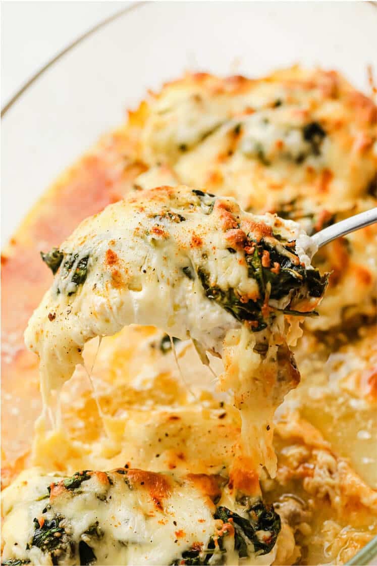 Creamy spinach chicken bake on a glass baking dish with a portion scooped up by a spoon.