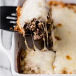 Philly cheese steak casserole on a baking dish with a serving scooped up by a spatula.