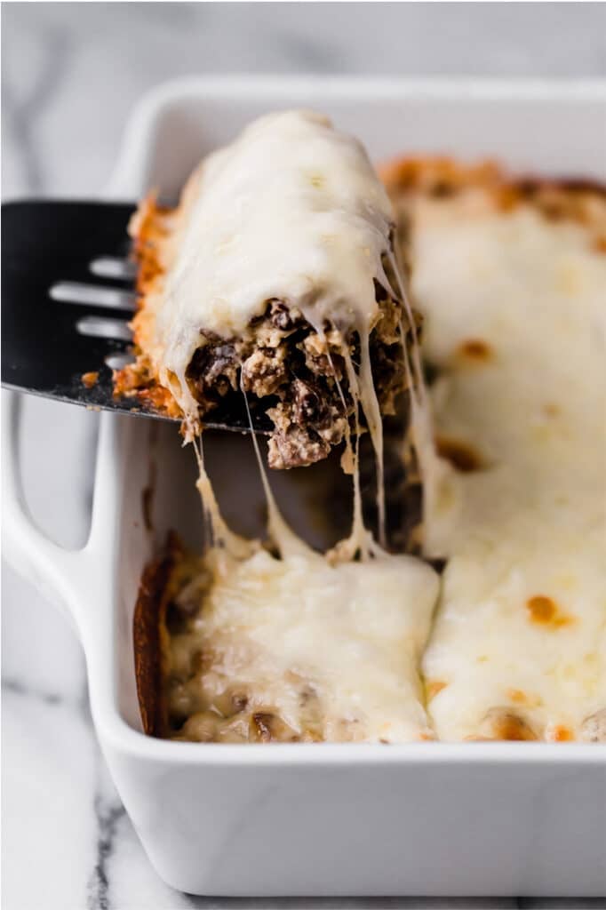Philly cheese steak casserole on a baking dish with a serving scooped up by a spatula.