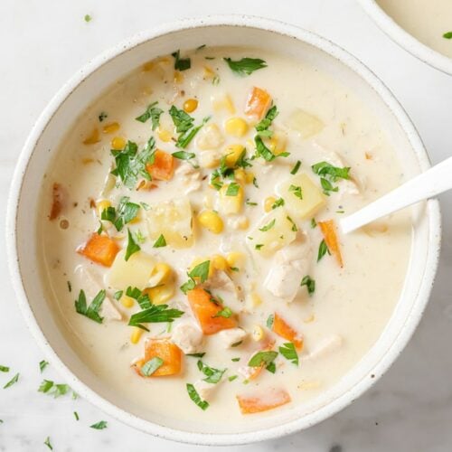 Garnished chicken corn soup in a bowl with a spoon.