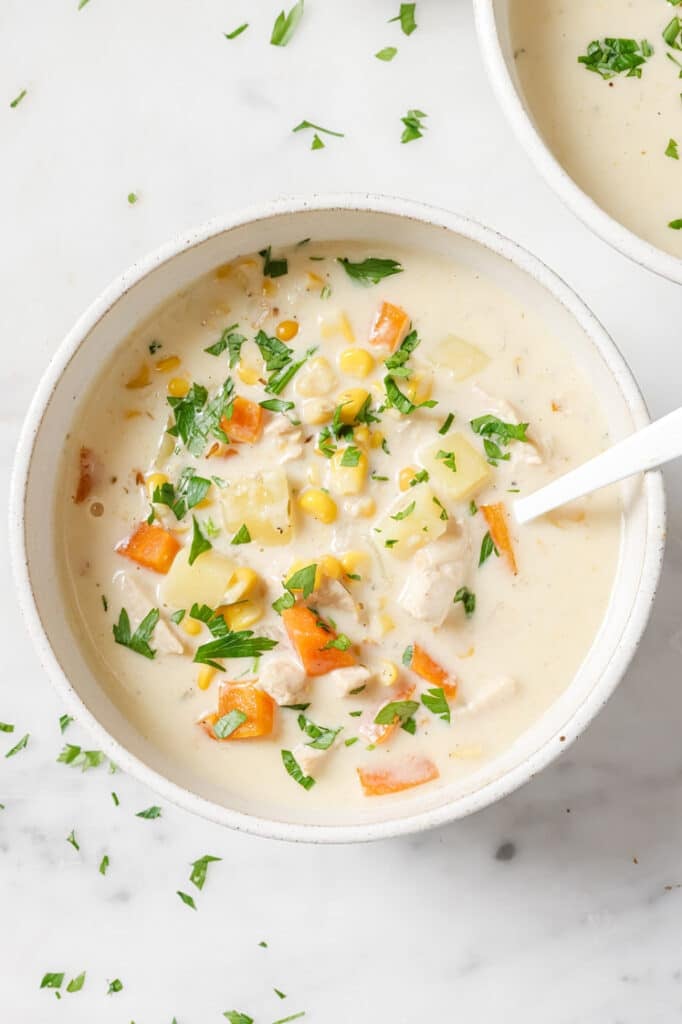 Garnished chicken corn soup in a bowl with a spoon.