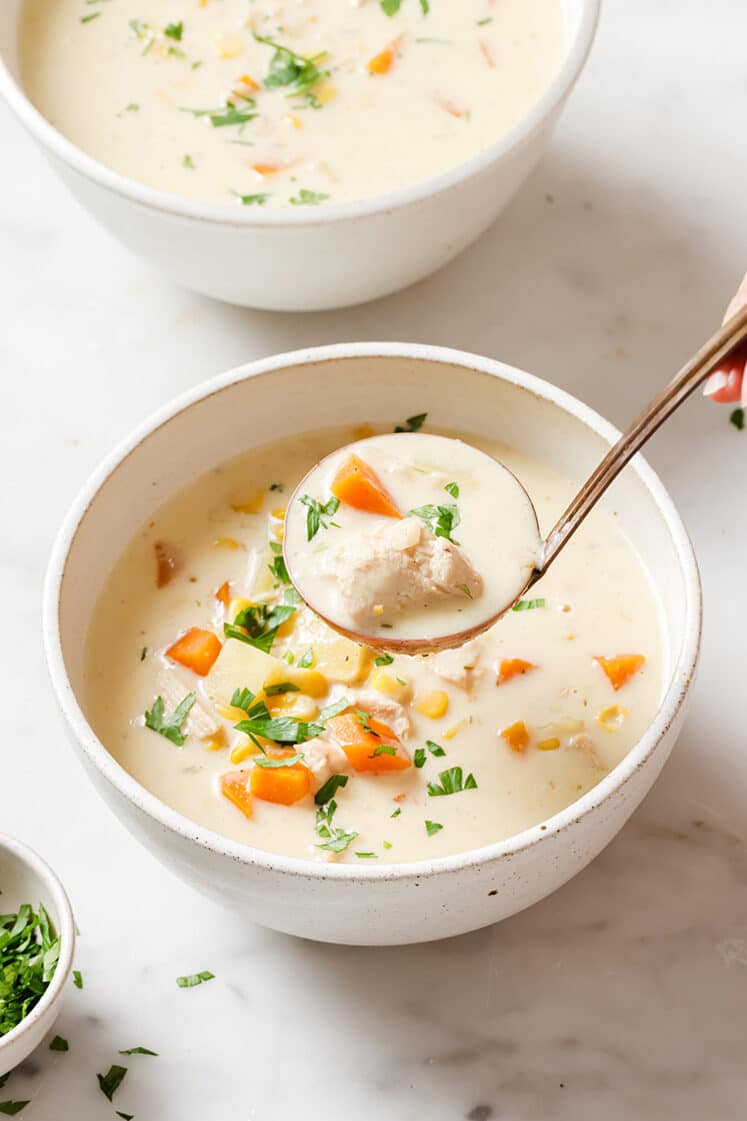 A bowl of chicken corn soup with a ladle.