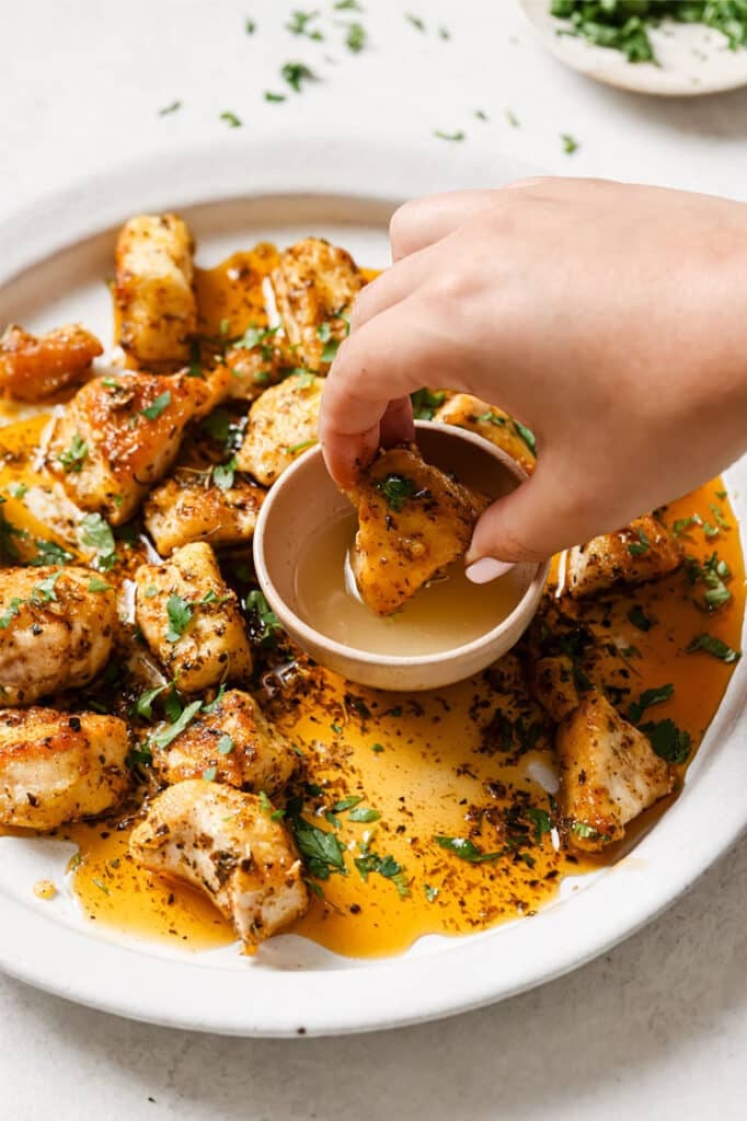 Garnished garlic butter chicken bites on a plate with a piece being dipped.