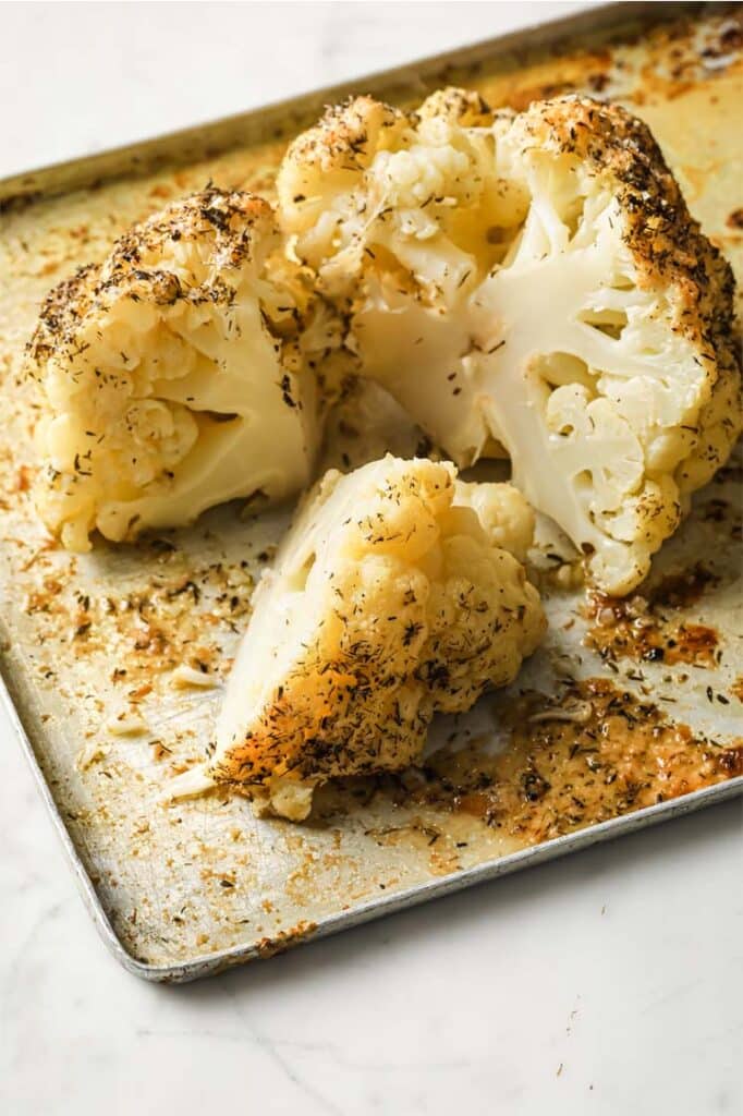 Sliced buttery whole roasted cauliflower on a baking sheet.
