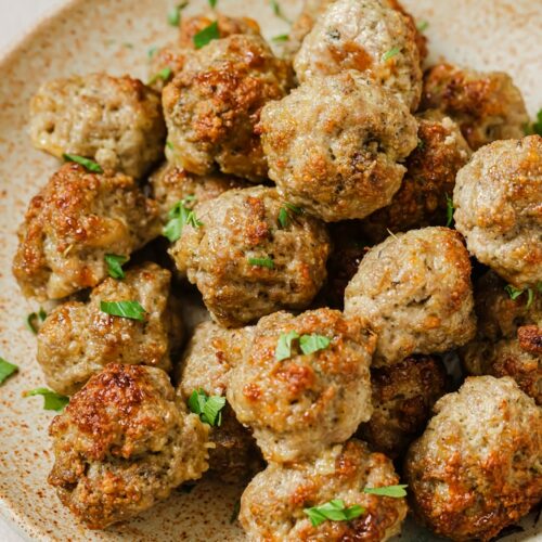 A plate of garnished sausage balls with cream cheese.