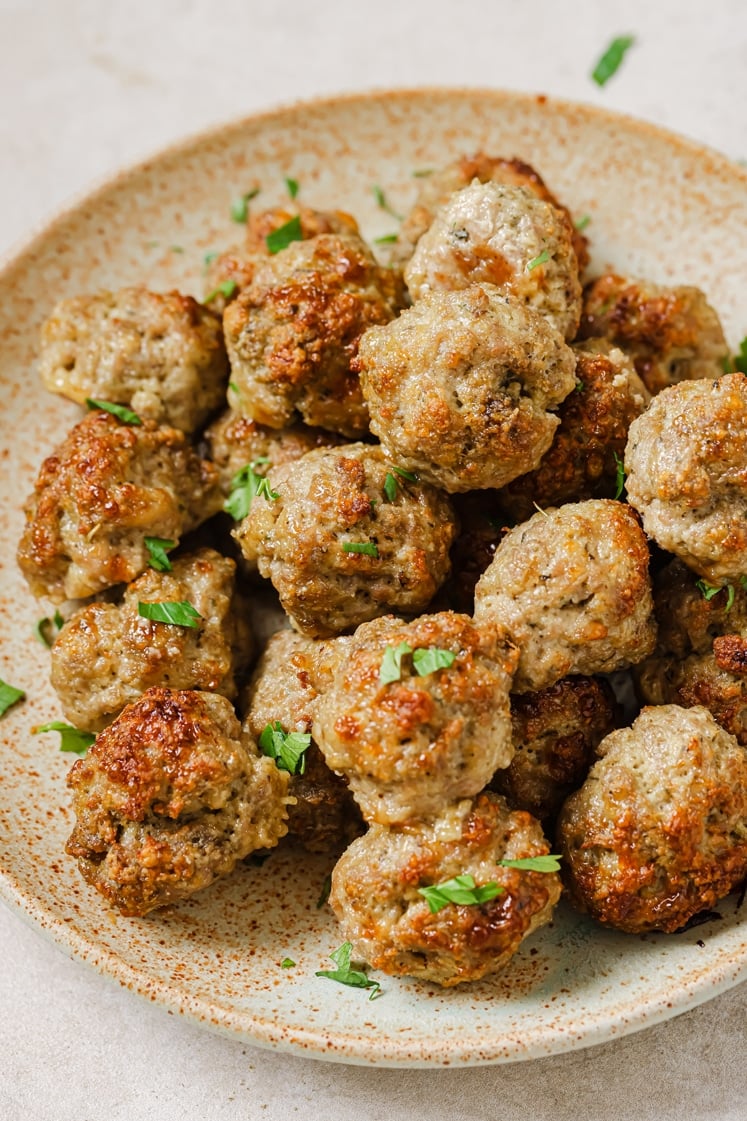 A plate of garnished sausage balls with cream cheese.