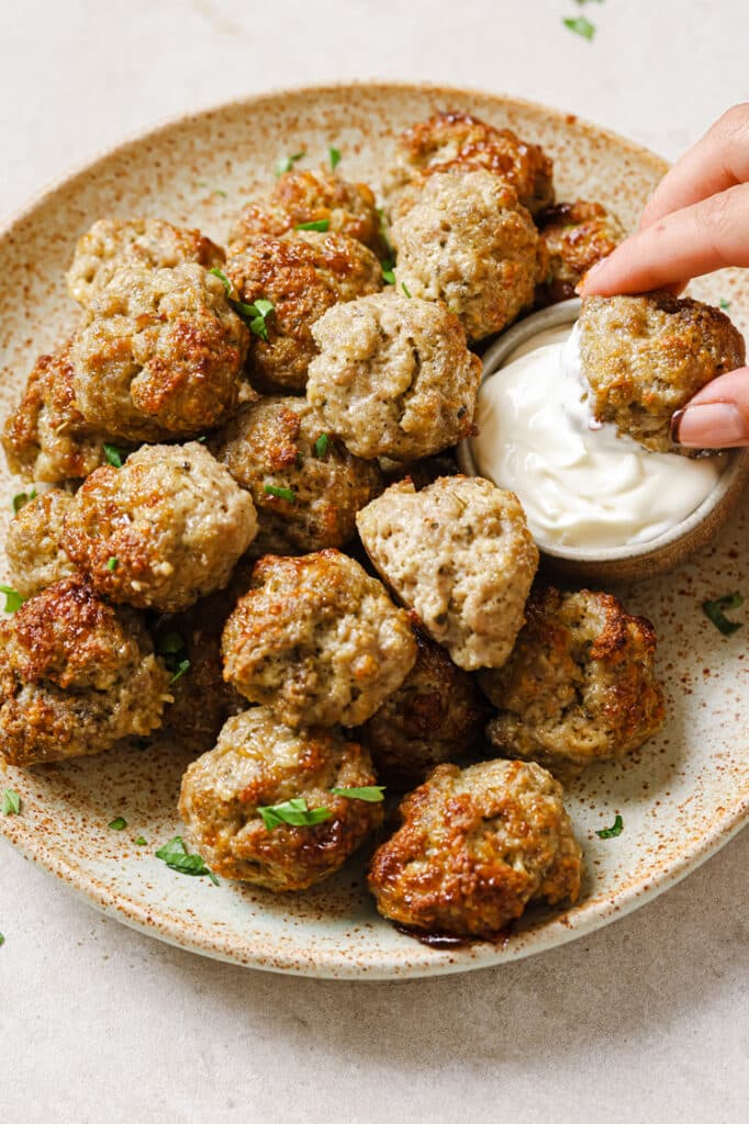 A plate of sausage balls with cream cheese with a piece being dipped in the sauce.