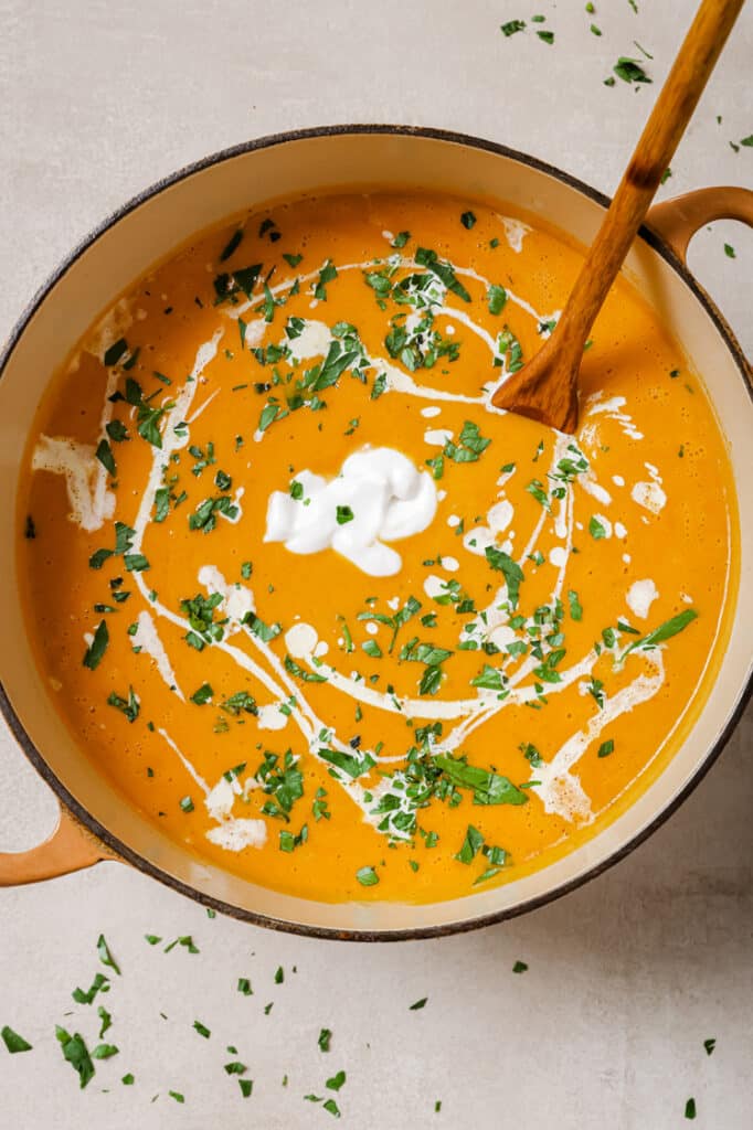 A pot of garnished sweet potato and red pepper soup with a wooden spoon.