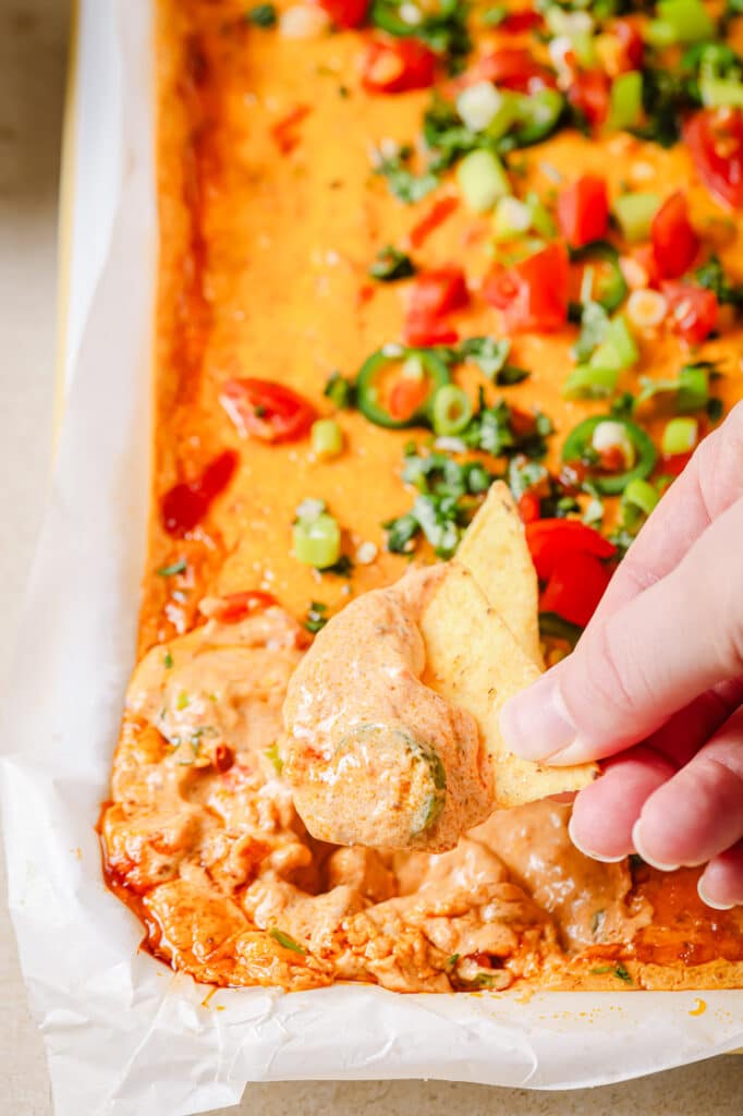 Chili cheese dip with a person dipping some tortilla chips.