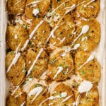 Garnished parmesan crusted potatoes on a baking sheet.