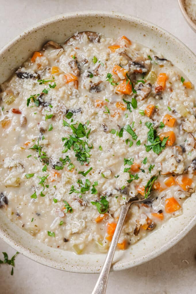 A bowl of garnished wild rice mushroom soup with a spoon.