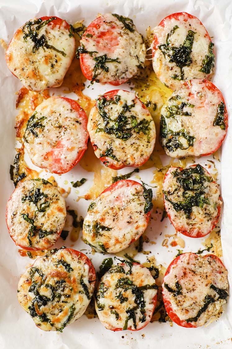 Baked tomatoes with parmesan and mozzarella cheese on a baking sheet.