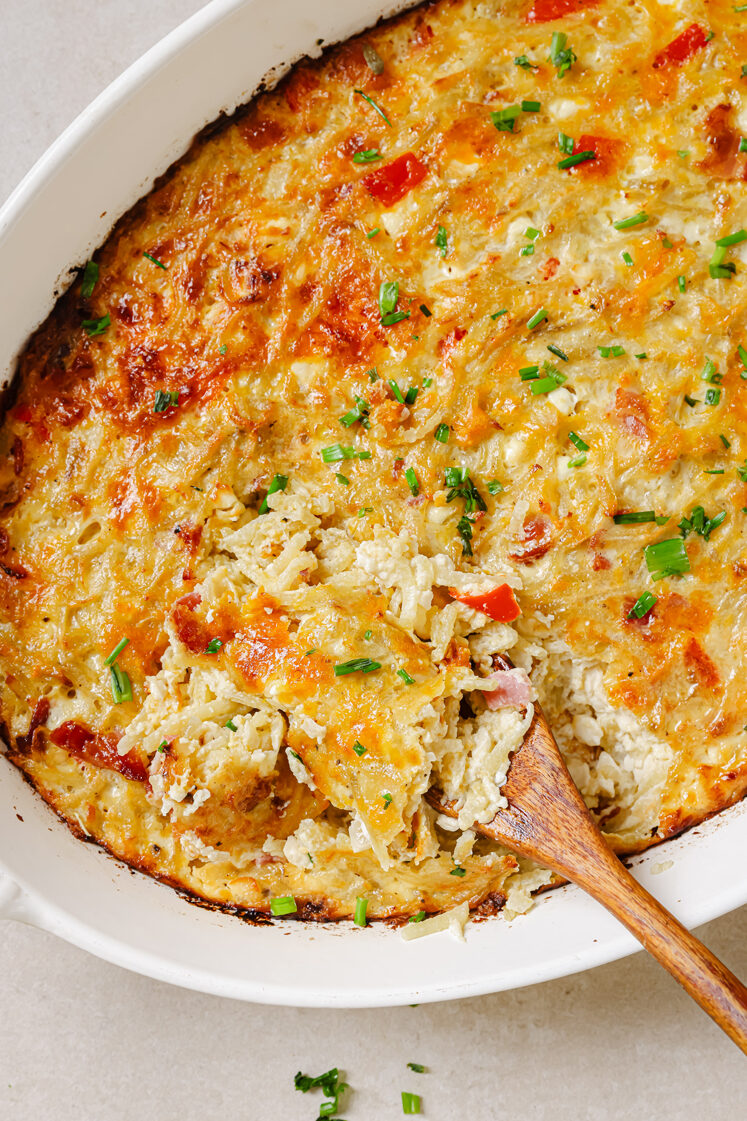 Hash brown breakfast casserole on a baking dish with a wooden spoon.