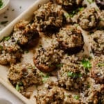 Garnished sausage stuffed mushrooms on a baking sheet.