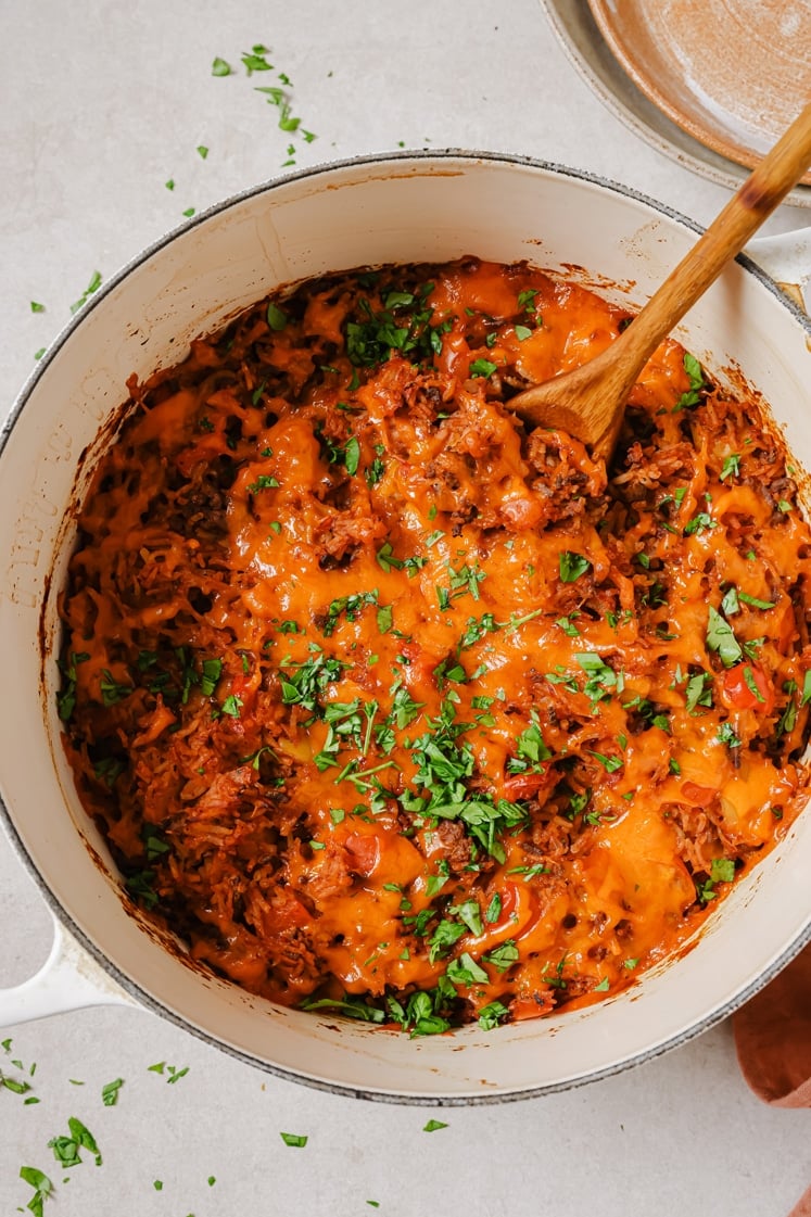 Garnished stuffed bell pepper casserole with a wooden spoon in a pot.