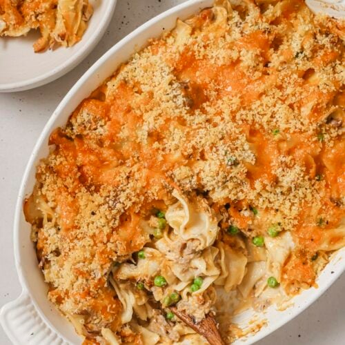 Tuna noodle casserole with a wooden spoon in a baking dish.