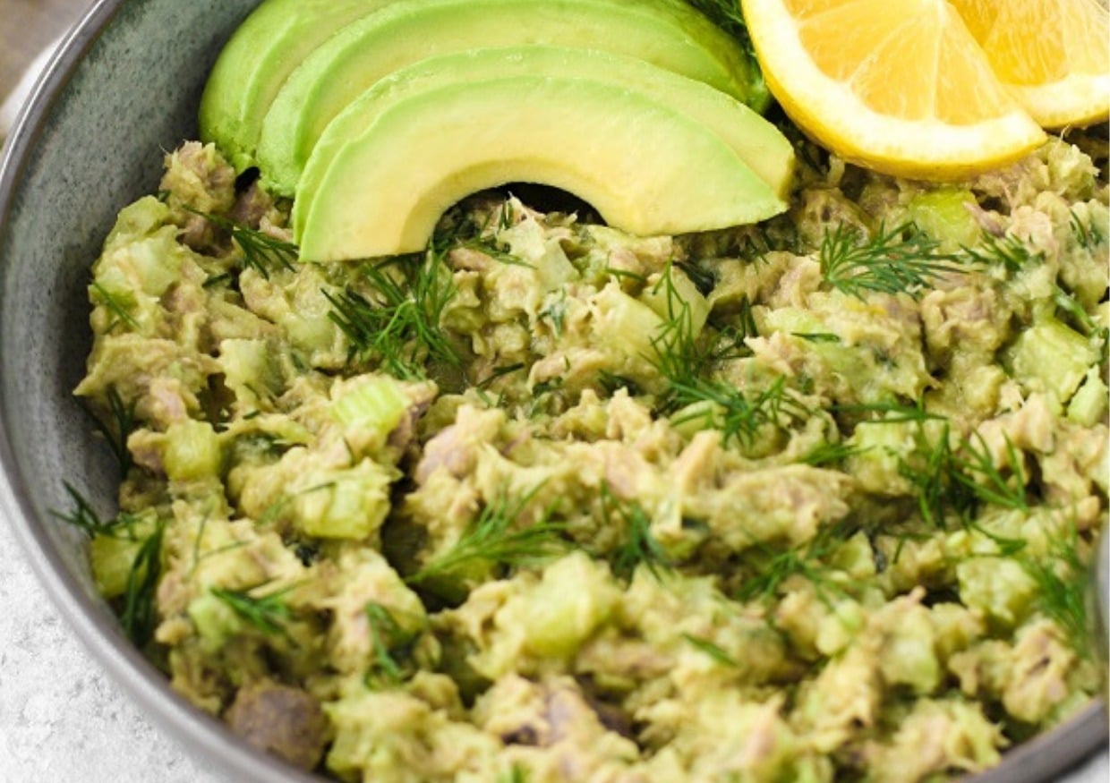 A bowl of avocado tuna salad with avocado slices and lemon slices.