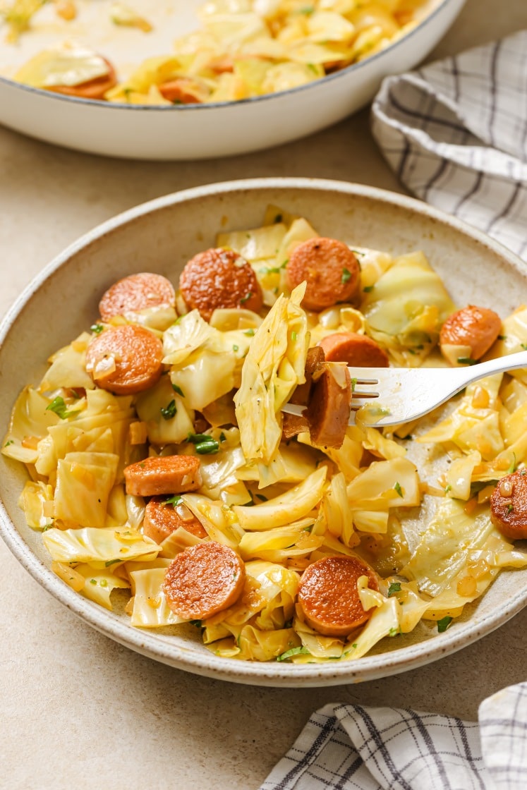 A bowl of cabbage and sausage with a fork skewering some.