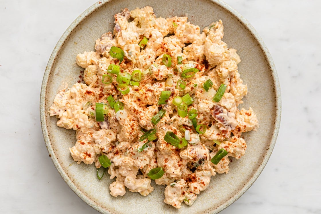 Cauliflower potato salad garnished with green onions in a bowl with a fork.