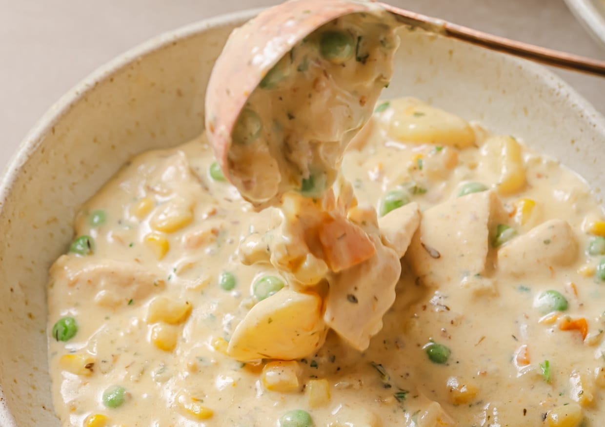 Chicken pot pie soup in a white bowl with a spoon.