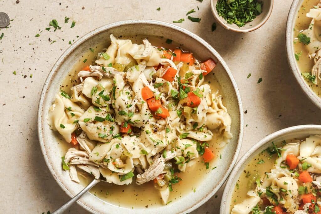 Homemade chicken tortellini soup with vegetables and herbs in a bowl.