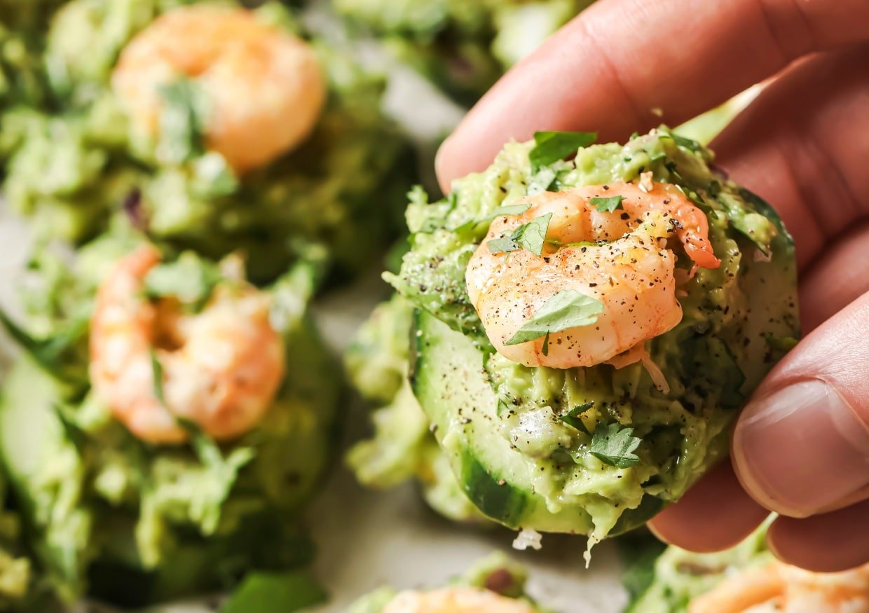 A person holding a cucumber with shrimp and guacamole.