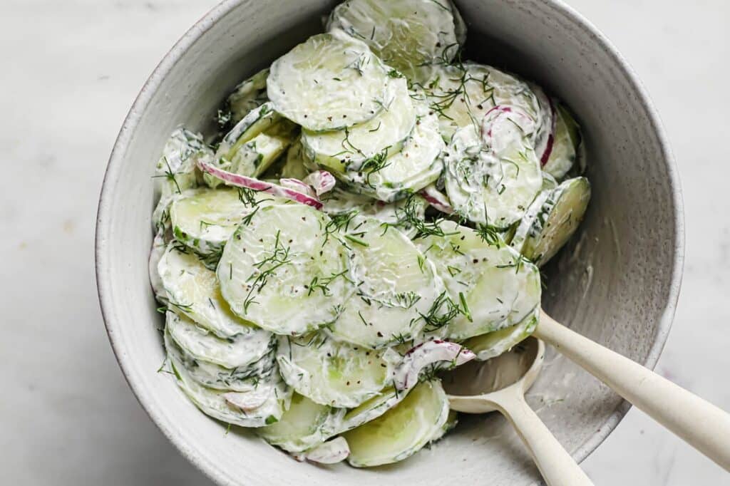 Creamy dill cucumber onion salad in a bowl with serving spoons.