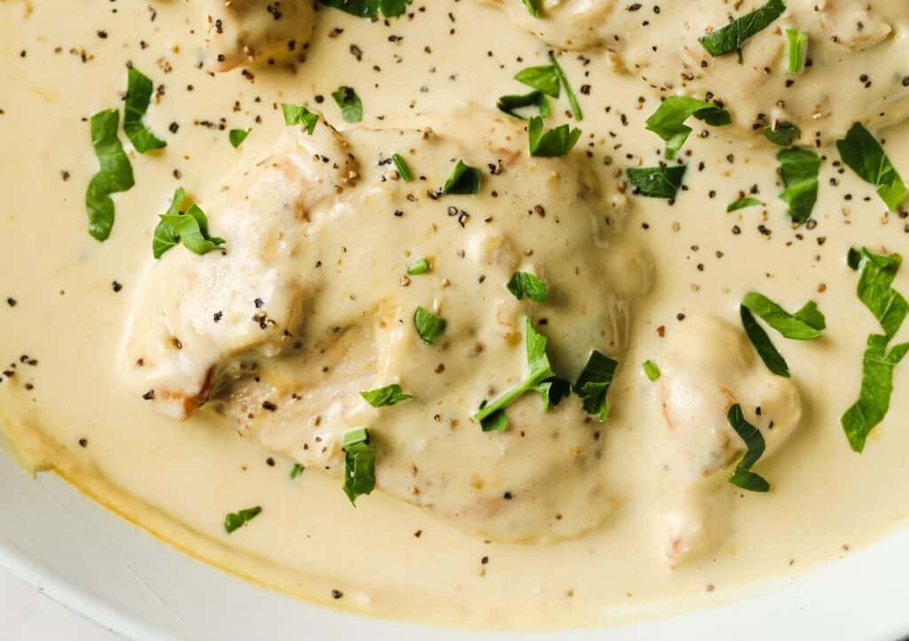 Creamy garlic chicken garnished with pepper and herbs in a skillet.
