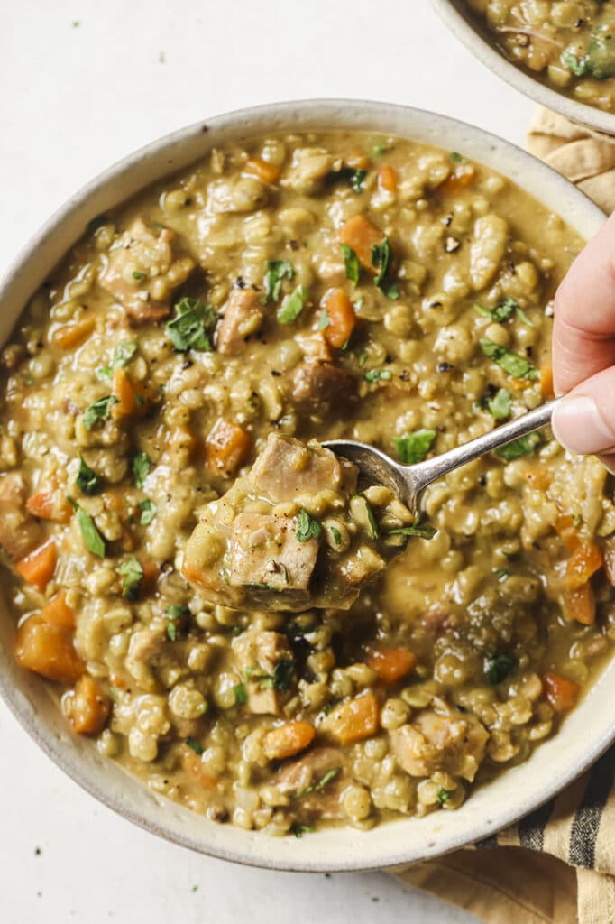 A spoonful held over the slow cooker split pea soup in a bowl.