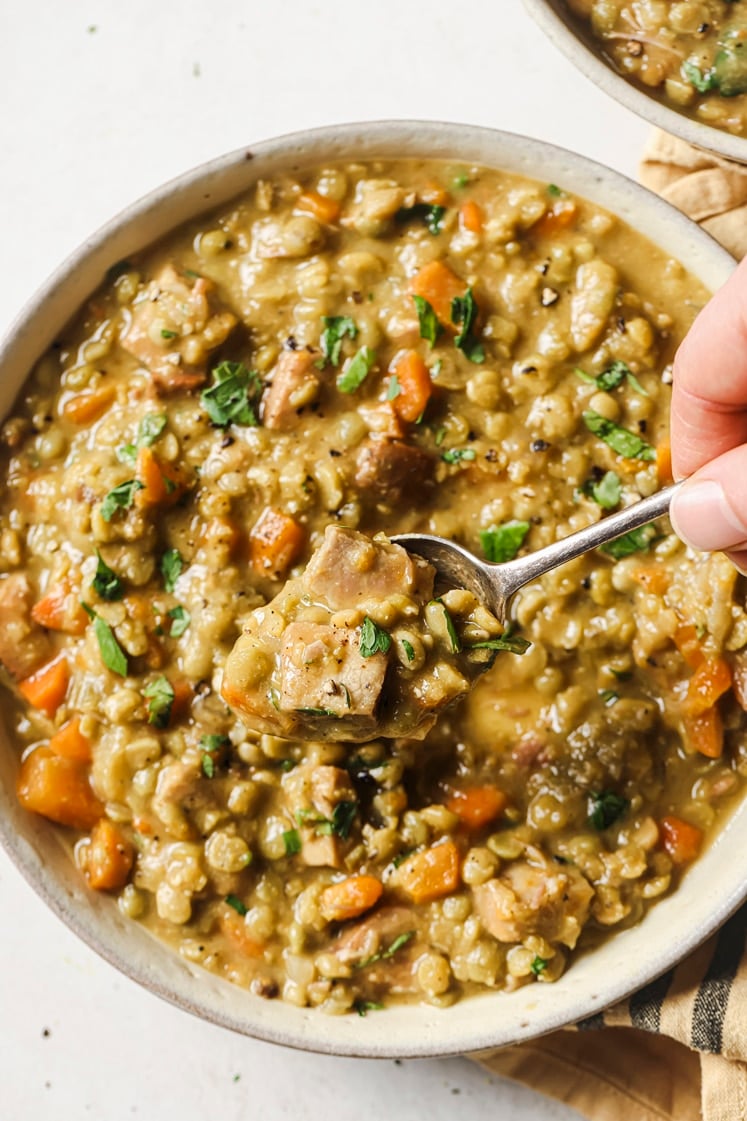 A spoonful held over the slow cooker split pea soup in a bowl.