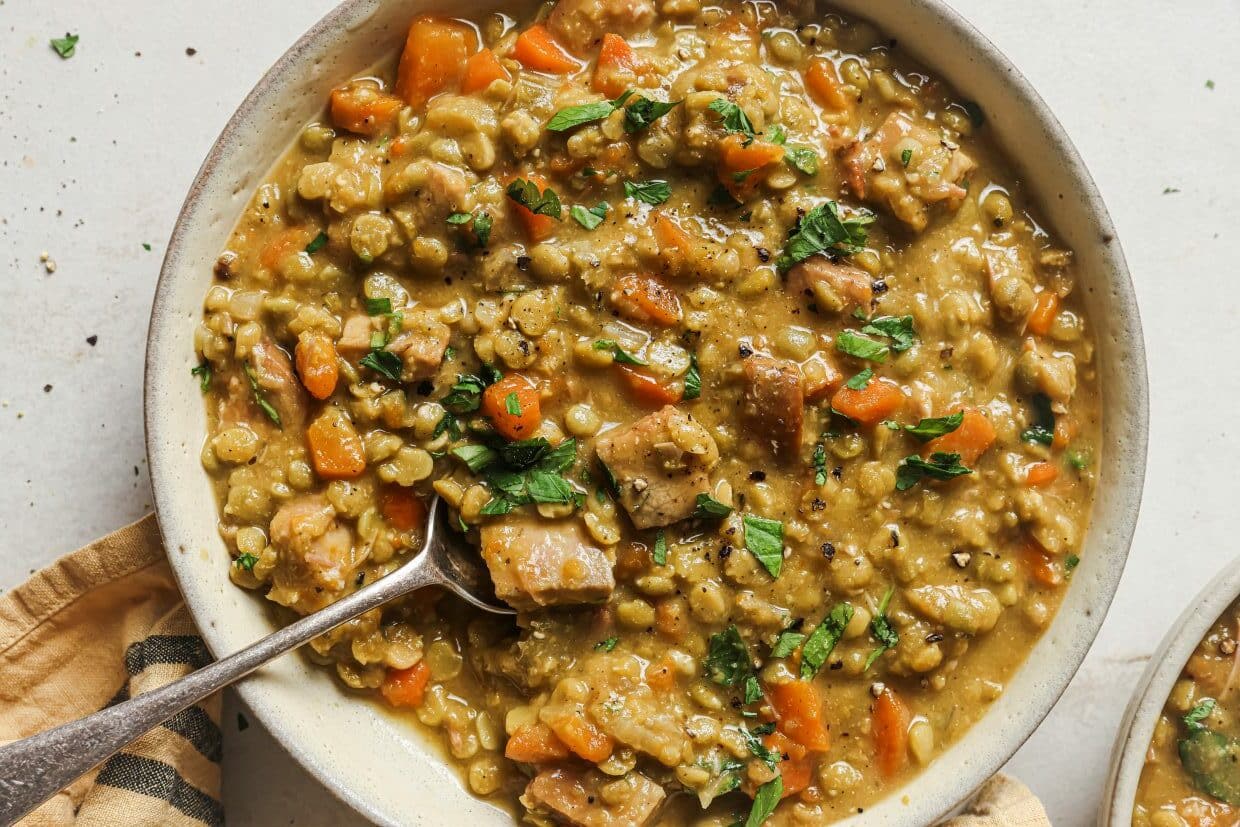 Slow cooker split pea soup garnished with fresh parsley in a bowl with a spoon.