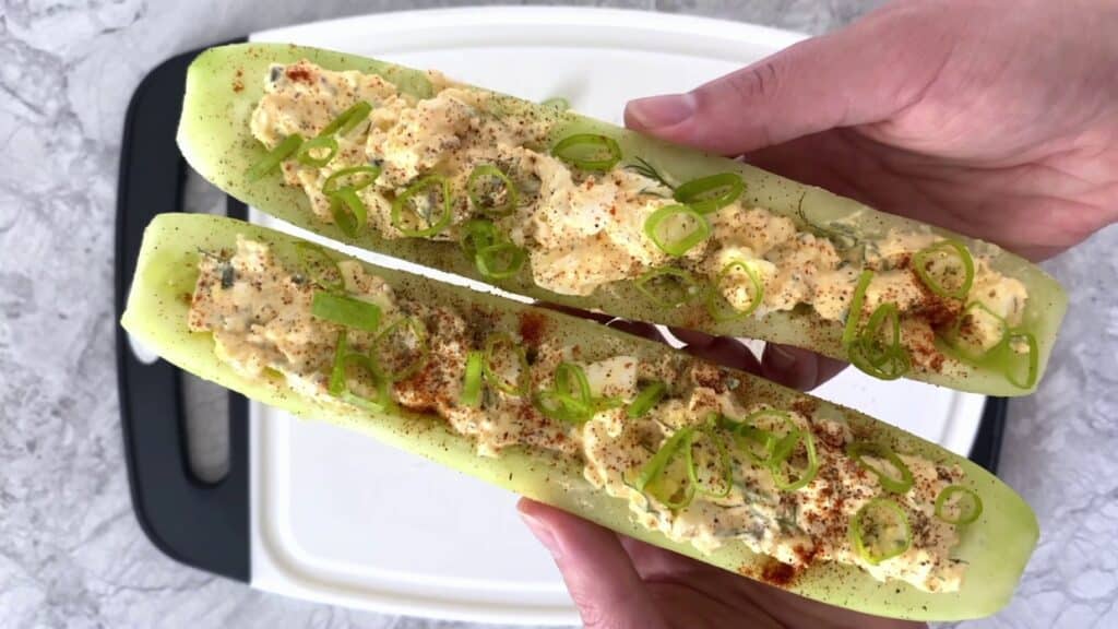 Spicy egg salad cucumber boats being held in two hands.