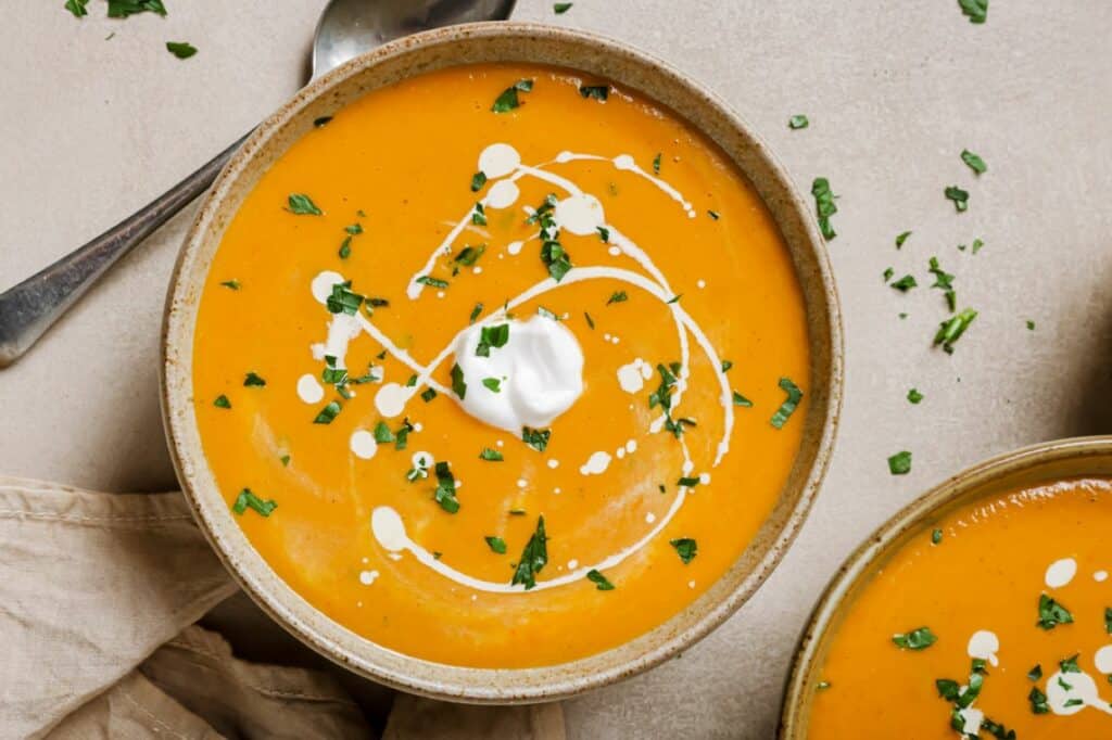 Two bowls of carrot soup with sour cream and parsley.