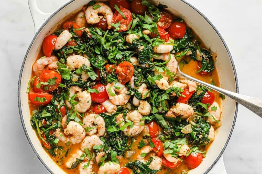 A bowl of Tuscan shrimp and spinach with a spoon.